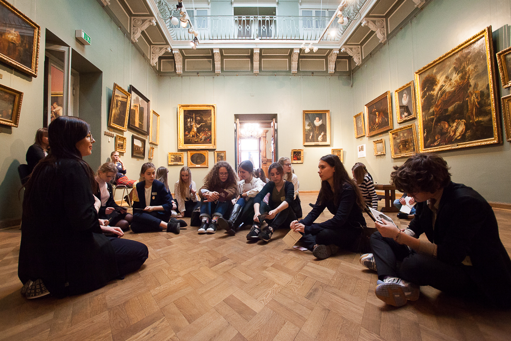 Фото. Група дітей з ведучою обговорюють музейні твори, сидячи на підлозі в залі музею