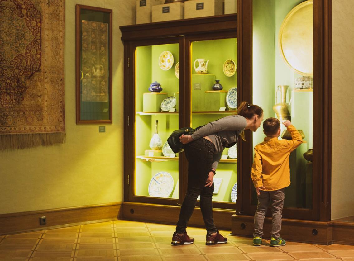 Photo. A boy is showing a woman an exhibit in a showcase in the hall of Islamic art.