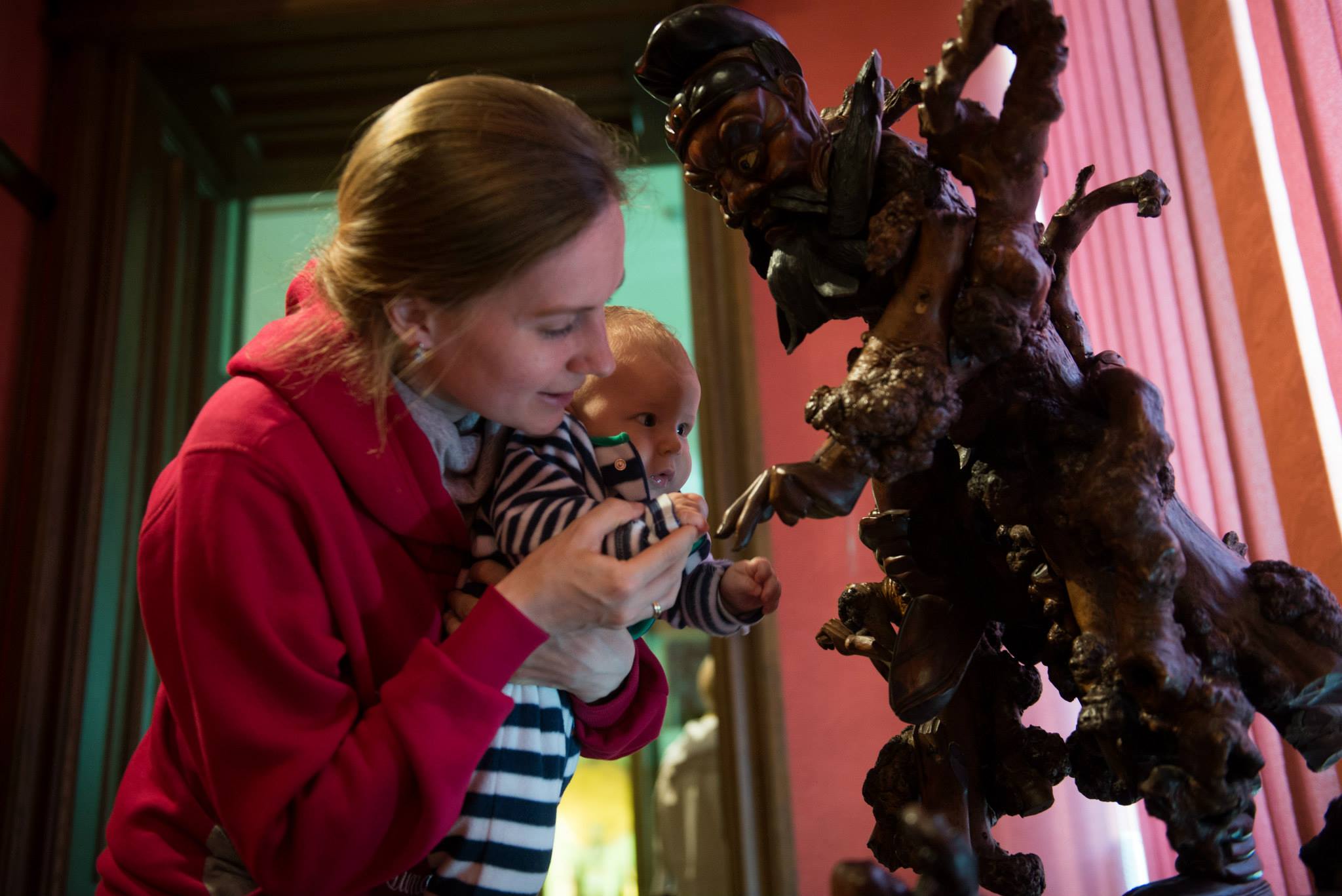 Photo. A woman is holding an infant in front of the wooden sculpture in the Chinese Art Hall.